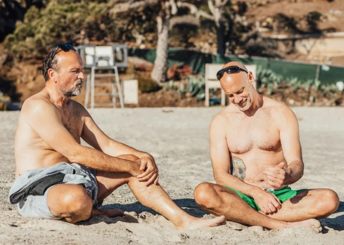 2 men sitting on the sand in the beach
