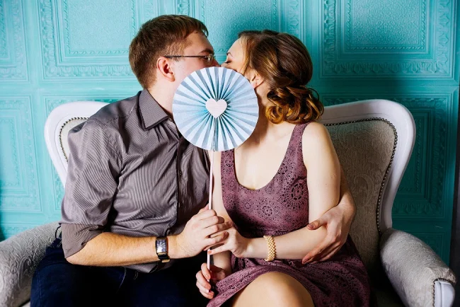 a man and woman kissing, with a blue paper fan cover their face