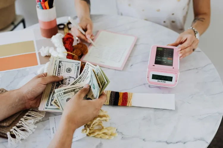 a white table with a pink calculate, with a person counting dollar bills and seem to be doing some budgeting