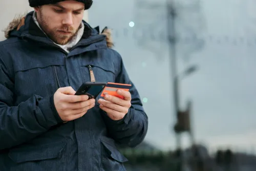 a man holding an orange card on his left side and a cellphone on right side, wearing winter clothes