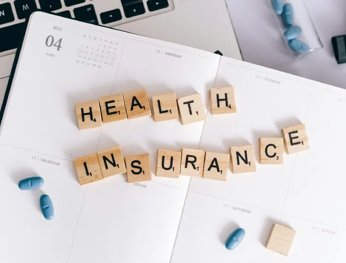 a paper with a scribble letters that says health insurance, above a white notebook